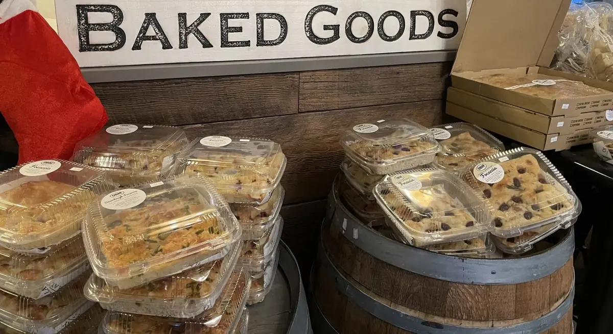 Trays of house sourdough focaccia stacked on barrels under a Baked Goods sign