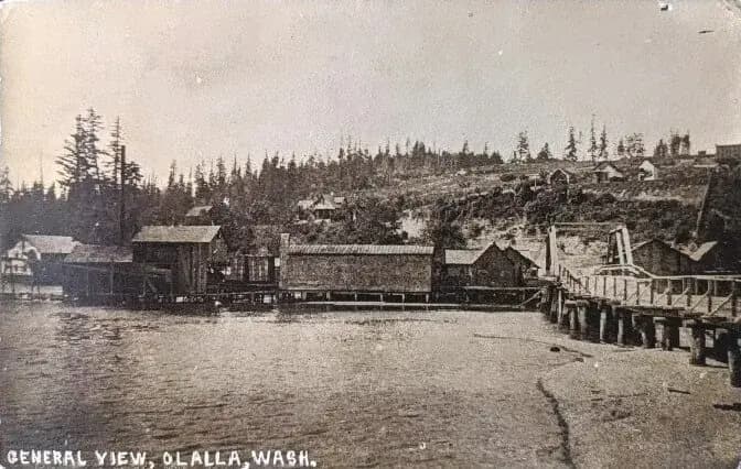 Old postcard captioned General View, Olalla, Wash., showing wooden buildings on piers along the shore with logged hills behind